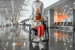 © Yakobchuk Olena - Young female worker of airport holding wheelchair with elderly lady in hall