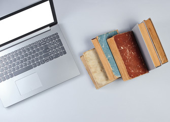 Wall Mural - Modern laptop and many old books on a gray background. Old and new sources of information. Top view