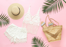 White Crochet Tank Top, Shorts, Straw Boater Hat, Wicker Beach Bag, Silver Glitter Flat Sandans, Tropical Palm Leaves On Pink Background. Overhead View Of Woman's Beach Outfit. Flat Lay, Top View.