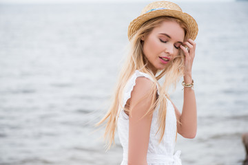 Wall Mural - pretty blonde woman with closed eyes touching hair near sea