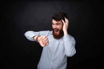 Photo of frustrated bearded guy, looking at watch, worried about his deadline, over dark isolated background