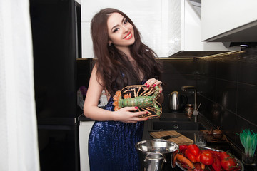 Portrait of a brunette girl in a chic new year's dress in a luxurious home interior. Prepares dinner and fresh lobster in the kitchen.