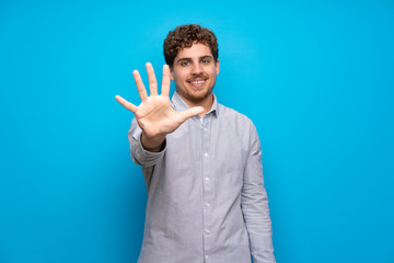 Wall Mural - Blonde man over blue wall counting five with fingers