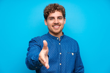 Wall Mural - Blonde man over isolated blue wall handshaking after good deal