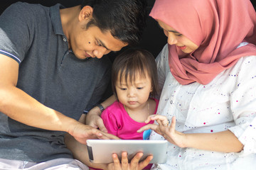 young muslim family , transport, leisure, road trip and people concept - close up portrait of happy man, woman and little girl sitting on trunk of hatchback car and playing tablet pc outdoors