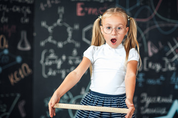 little blonde girl with a surprised face with a ruler in her hands pupil girl with big rulers agains