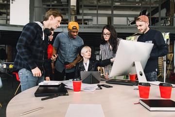 Wall Mural - Young six people working in positive environment in loft office, woman sitting at the table and using computer