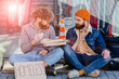 © Iryna - Homeless beggar and young handsome beard man listening to his story sitting together on the ground outdoors. Concept of human understanding