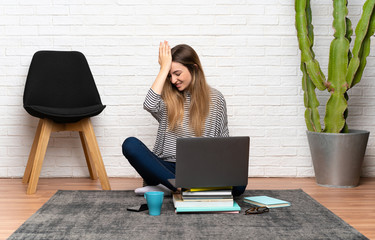 Young woman sitting on the floor with her laptop having doubts with confuse face expression