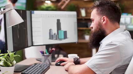Talented bearded architect working in 3D software to design new buildings. In the background - production media house