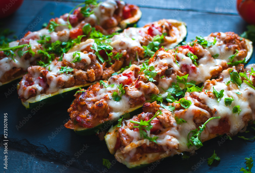 Close-up of stuffed zucchini boats with ground beef, spicy tomato sauce, cheese and fresh parsley, on dark background - obrazy, fototapety, plakaty 