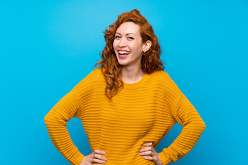 Redhead woman with yellow sweater posing with arms at hip and smiling