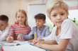 © Ihor - Charming little blond haired girl looking to the camera during art class, copy space. Adorable schoolgirl enjoying drawing at elementary school lesson