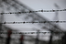 Barbed Wire With The Blurred Background Of A Refugee Camp
