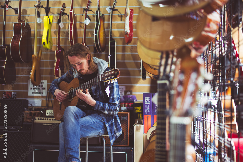 Mężczyzna gra na gitarze w sklepie muzycznym - obrazy, fototapety, plakaty 