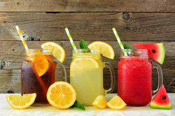 Wall Mural - Variety of summer drinks in mason jar glasses with fruit against a dark wood background. Iced tea, lemonade and watermelon juice.