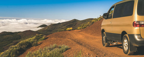 Off road vehicle on a mountain path. Blue sky, clouds and a beautiful panorama on the background. 4x4 van on a dirt road. Suv climbing on a tourist rural way Travel adventure and open air trip concept