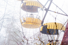 Selective Focus Of Yellow Ferris Wheel Attraction In Fog In Abandoned Amusement Park Overgrown With Trees In Pripyt, Chernobyl Zone Of Alienation