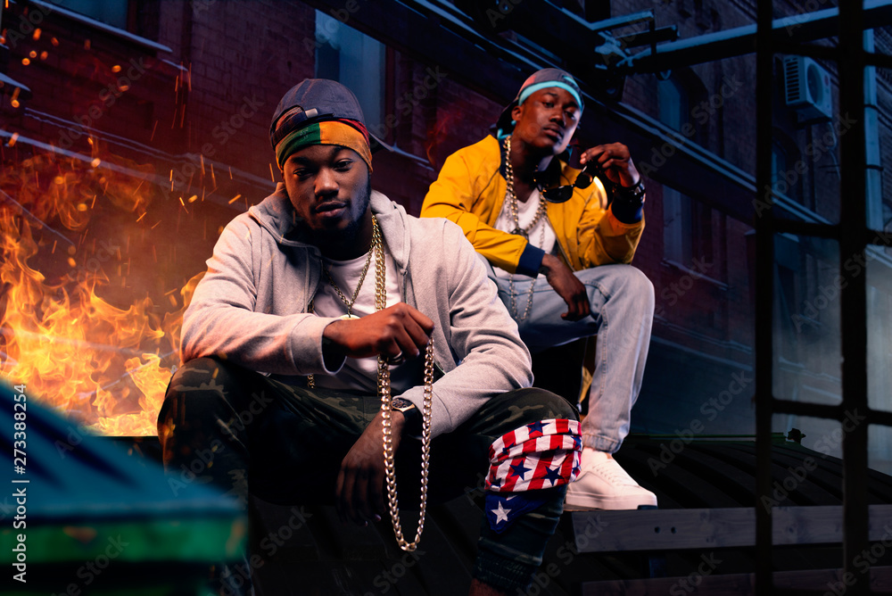 Two black rappers in caps sitting by the fire - obrazy, fototapety, plakaty 