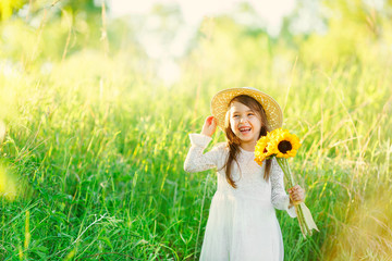 Portrait of little girl with a bouquet of wild yellow flowers standing and smiles in the meadow sunny summer day in a straw hat. Copy space.