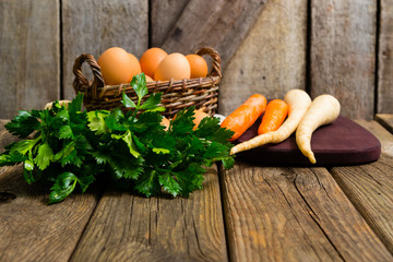 Poster - basket of eggs and carrots, parsley roots, celery, cutting board, old weathered wooden background