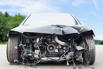 Front view of crashed car with damaged car parts against green bushes and blue sky, car crash accident on the street