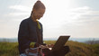 © Lalandrew - young girl working at laptop with earphones in the fields