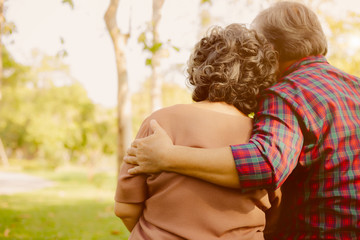 Wall Mural - Elderly man or senior guy embracing wife or elderly woman with love. Grandfather always concerned or care his grandmother. They are romantic couple. Father and mother stay together at park copy space