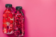 Detox Infused Fresh Water With Strawberry Raspberries In Sparkling Glasses And Bottle On  Colorful Pink Background, Copy Space. Cold Summer Drink. Mineral Water. Top View, Flat Lay 