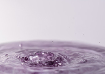 Close up macro photography of a purple water drop splashing into water with a light colored white gray background