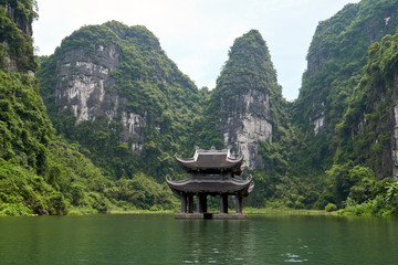 Wall Mural - Small temple on the river surrounded by karst mountains. Beautiful landscape during the Trang An boat tour in Tam Coc, Vietnam.