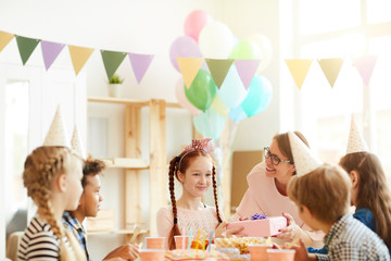 Wall Mural - Multi ethnic group of children celebrating birthday sitting at table in cafe, focus on happy red haired girl, copy space