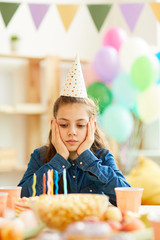 Wall Mural - Portrait of sad teenage girl sitting alone at party table on her Birthday