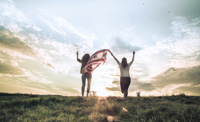 Young happy girl running and jumping carefree with open arms over wheat field. Holding USA flag.