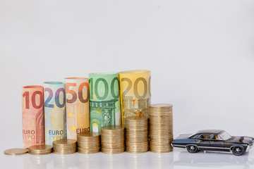 A black model of a car and ten, twenty, fifty, one hundred, two hundred and coins euro rolled bills banknotes on white background. Histogram from the euro. Concept of currency growth, savings.