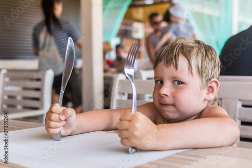 Fotografía A little boy holds a knife and fork and waits for food