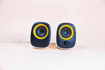 Two black and yellow speakers are standing on a pink surface