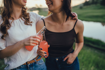 close up. two hands of girls hold bottle, girls have fun in the summer, drinking cocktail, at sunset, positive facial expression, outdoor