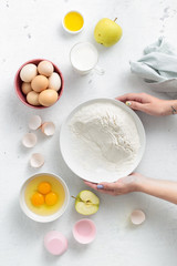 Poster - Person cooking dessert. Women hands preparing apple pie on a white background top view. Baking food ingredients