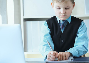 Confident executive businessman boss boy making notes sitting at the desk with laptop in office.