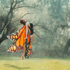 attractive slender girl with braided dark hair in a black chic body and light bright butterfly wings flies up into the air, the joy of warm summer days, the first flight of moth, lightness and grace