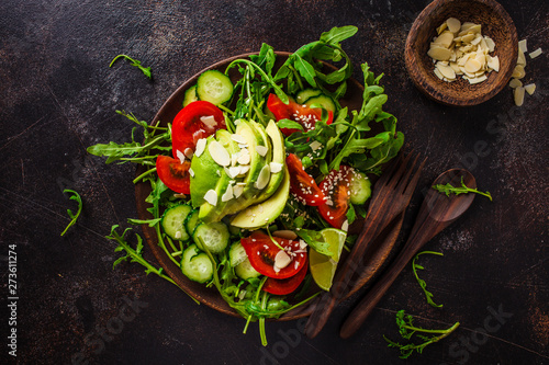 Fotomural Green salad with avocado, tomatoes, cucumbers and nuts in wooden plate on dark background