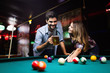 © NDABCREATIVITY - Young couple playing snooker together in bar