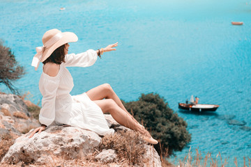 Wall Mural - Happy asian woman travels in Greece. Having fun at the stunning view on sea resort and old town of Lindos on the mountain