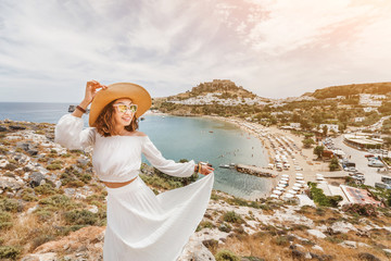 Wall Mural - Happy asian woman travels in Greece. Having fun at the stunning view on sea resort and old town of Lindos on the mountain