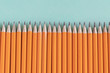 Border of sharpened orange pencils against a blue green background, with copy space