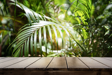 Wall Mural - Dark wood table top (Bar) with blur on green palm leaves or tree in tropical forest with bokeh light at background