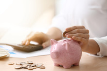 Young Woman Putting Coin In Piggy Bank On Table, Closeup