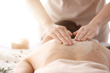 Young woman undergoing treatment with body scrub in spa salon, closeup