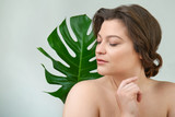 Fototapeta  - Portrait of beautiful plus size woman with tropical leaf on light background